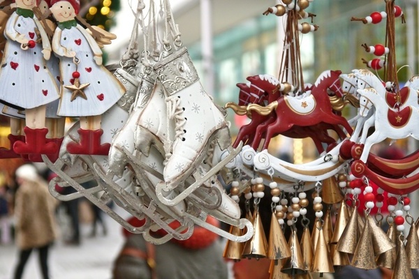 Rot-wei&szlig;e Engel- und Schlittschuhfiguren sowie Schaukelpferde mit Gl&ouml;ckchen aufgeh&auml;ngt an einem Weihnachtsmarktstand