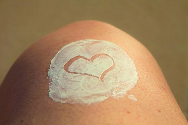 Haut, die sichtbar mit Sonnencreme eingeschmiert ist. In die Creme ist ein Herz gezeichnet.