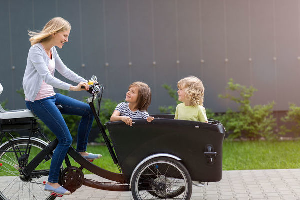 Eine Frau f&auml;hrt auf einem Lastenrad. Im Lastenkorb sitzen zwei Kinder