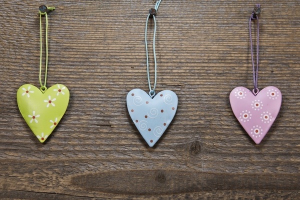 Drei bunte herzf&ouml;rmige Anh&auml;nger vor h&ouml;lzernem Hintergrund