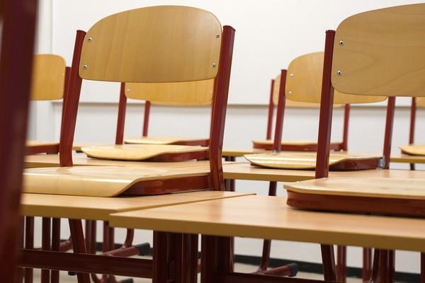 Holzst&uuml;hle auf Schultischen in einem Klassenzimmer