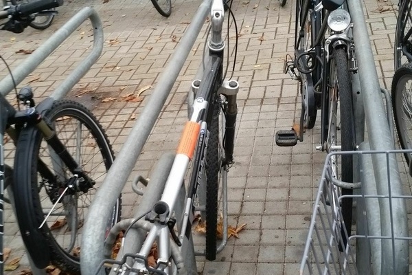 Mehrere abgestellt Fahrräder, ein Fahrrad mit rotem Aufkleber auf der Stange eines silbernen Herrenfahrrads