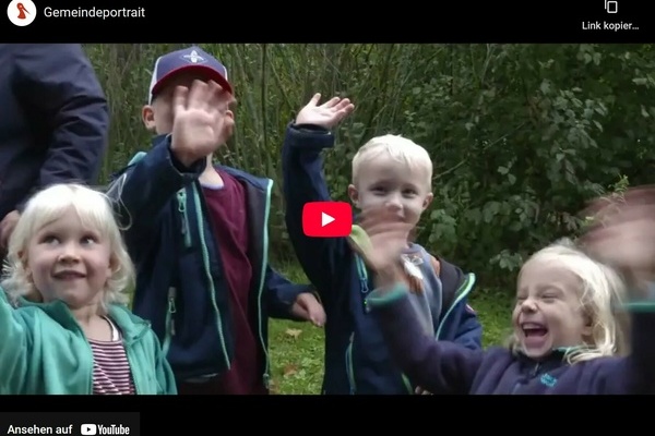 Szene aus dem neuen Denzlinger Gemeindeportrait: winkende Kinder, im Hintergrund gr&uuml;ne Str&auml;ucher