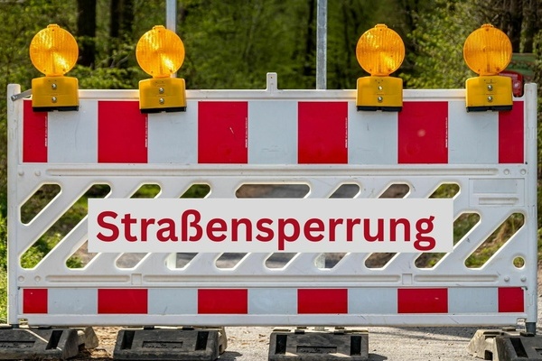 Stra&szlig;ensperrung - rote Schrift auf wei&szlig;em Untergrund und Verkehrsabsperrung mit organgenen Warnleuchten