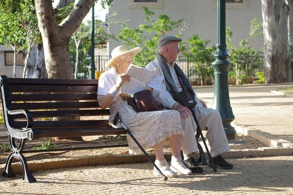 Zwei ältere Personen mit Gehstöcken sitzen auf einer Ruhebank