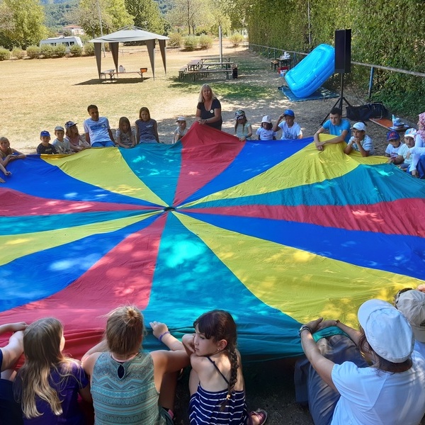 Alle teilnehmenden Kinder und Beteuer/-innen halten eine groe runde, farbige Plane